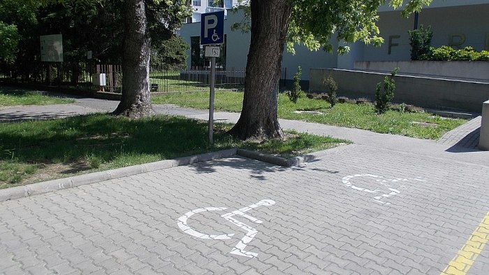 Pflasterstein-Fläche mit Rollstuhlsymbol am Boden und einem Schild, das ein großes P und ebenfalls ein Rollstuhl-Symbol zeigt.
