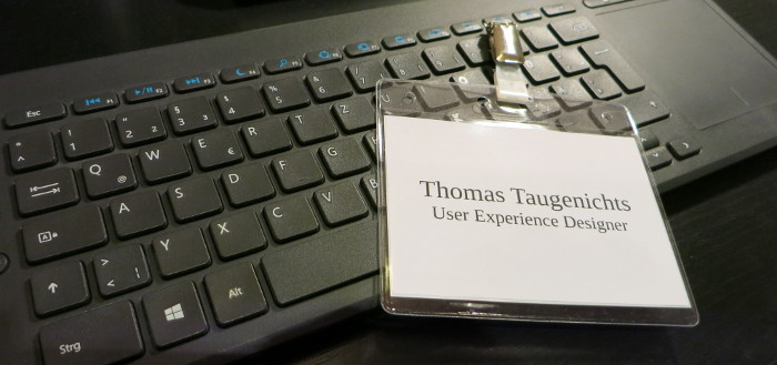 Tastatur und Namensschild mit Beschriftung »Thomas Taugenichts, User Experience Designer«.