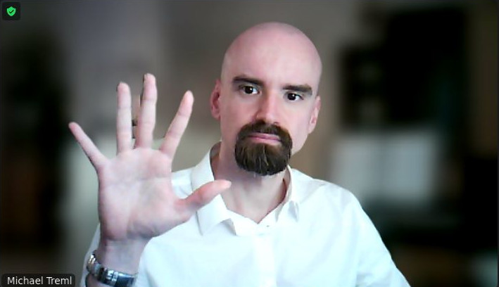 Ich vor einem verschwommenen Hintergrund. Ich habe eine Hand mit gespreizten Fingern vor mir und zwischen zwei der Finger ist der Hintergrund nicht verschwommen.