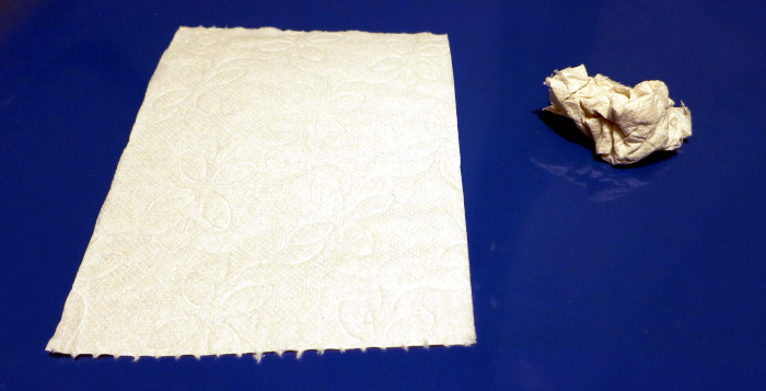 Ein zerknülltes neben einem unzerknülltem Blatt Toilettenpapier. Das zerknüllte Blatt nimmt nur einen Bruchteil des Platzes ein, den das unzerknüllte braucht.