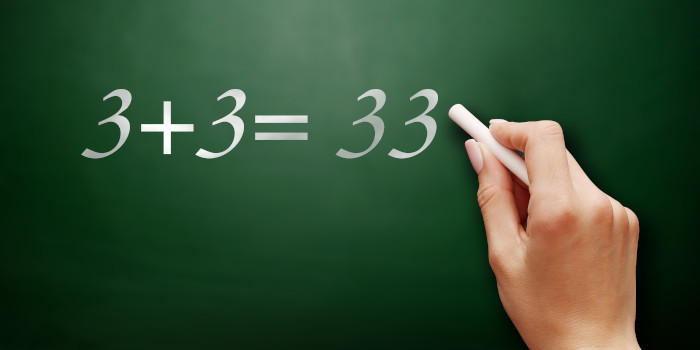 Grüne Schultafel, auf die eine Hand mit Kreide schreibt: »3 + 3 = 33«.