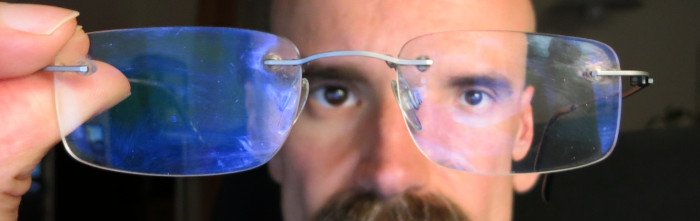 Brille etwas weiter vor einem Gesicht gehalten, sodass nur eines der Augen hinter einem Brillenglas liegt und dadurch deutlich kleiner aussieht als das andere Auge.