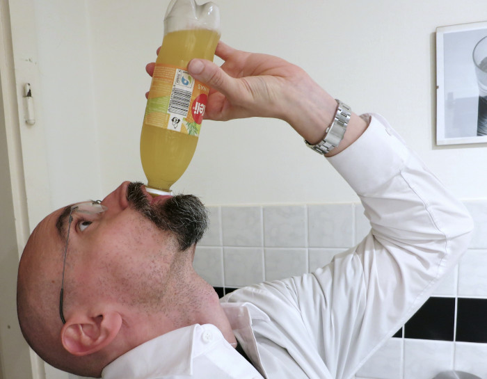 Nach oben geneigter Kopf mit voller, senkrecht gehaltener Plastikflasche im Mund.