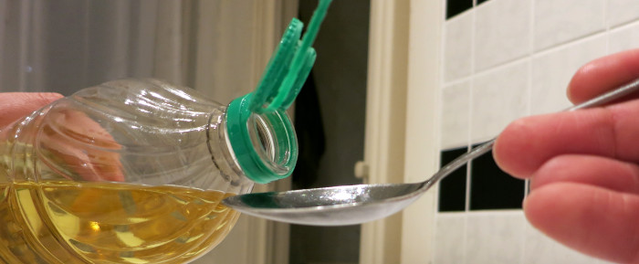 Esslöffel unter Öffnung einer gekippten Ölflasche.