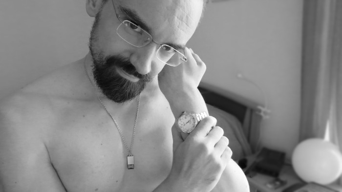 Schwarzweißfoto, auf dem ich bei nacktem Oberkörper Brille, Kette und Armbanduhr trage.